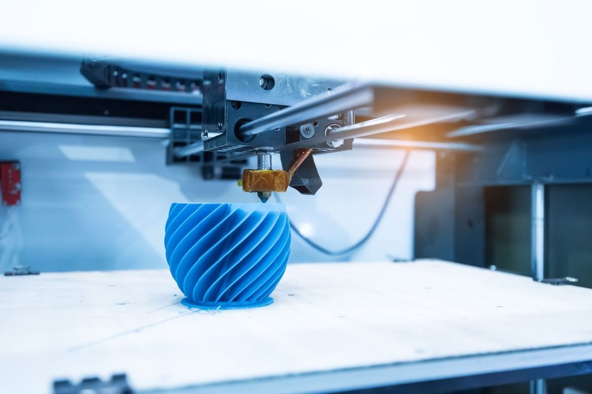 A 3D printer actively creating a detailed blue, spiraled vase-like object on its build plate, with the nozzle visible and a subtle warm light emanating from the printer's interior. This image illustrates the innovative process of additive manufacturing, a key focus for investors in the rapidly growing 3D printing sector.